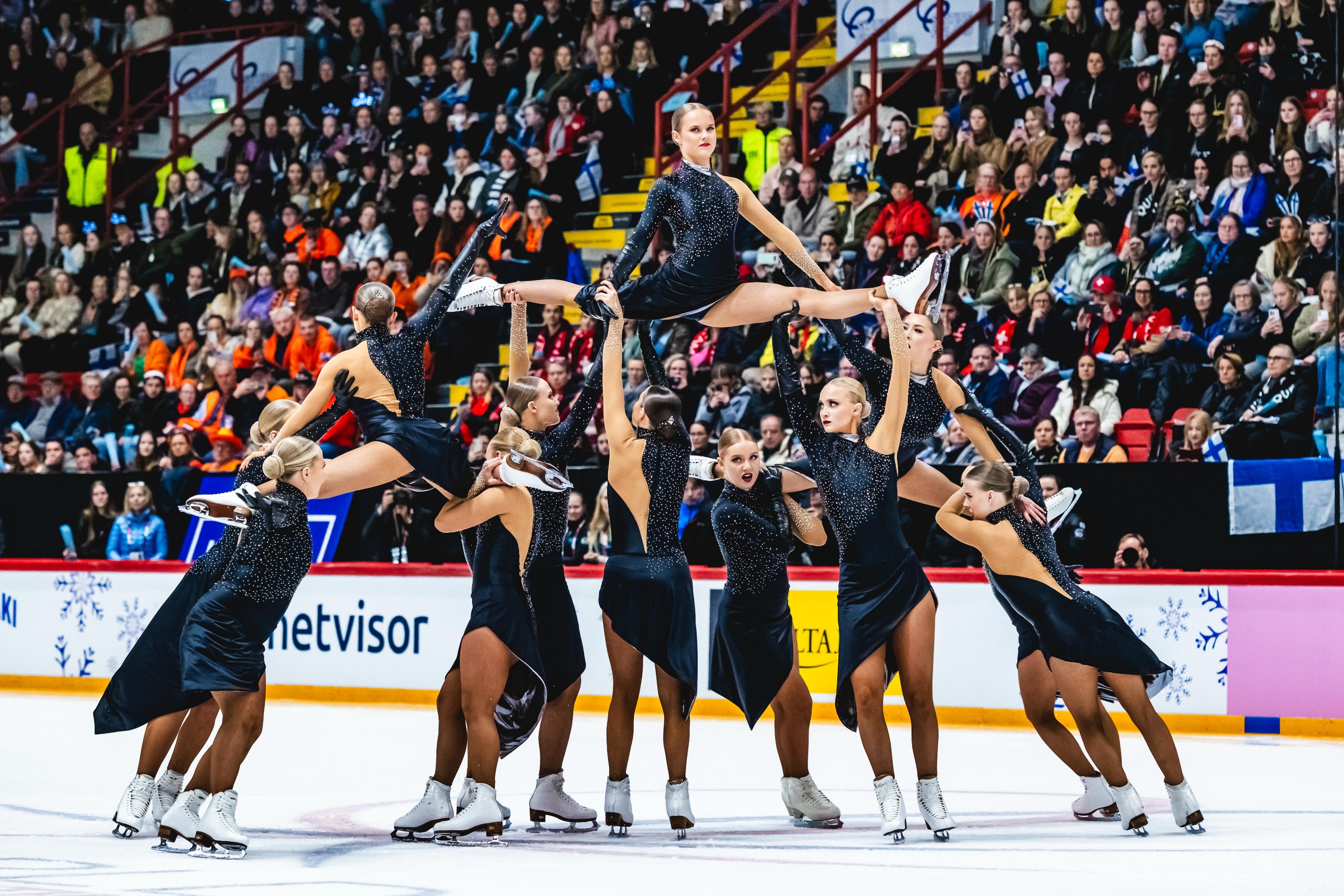A group of women in black dresses on ice with a crowd watchingAI-generated content may be incorrect.