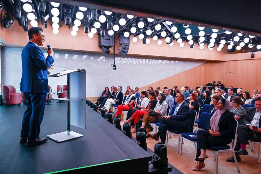 A person speaking into a microphone on a stage with a crowd of peopleAI-generated content may be incorrect.